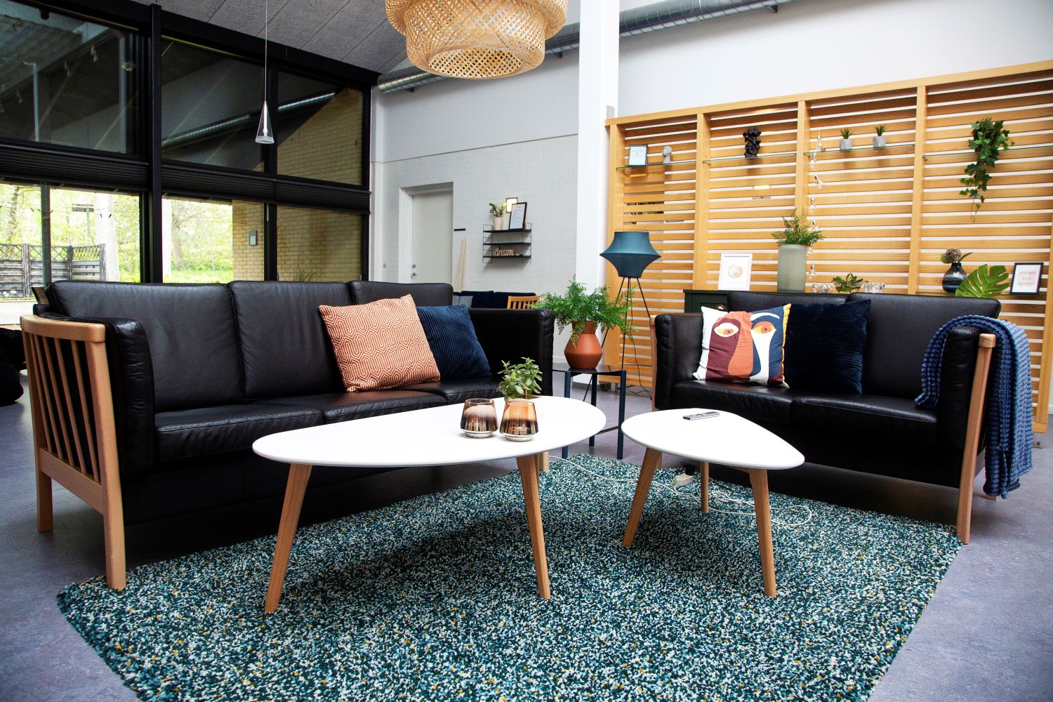 Dagligstue med to sorte sofaer grønt guldtæppe hvide sofaborde, det ene bord med to brune lysestager og en lille grøn plante på