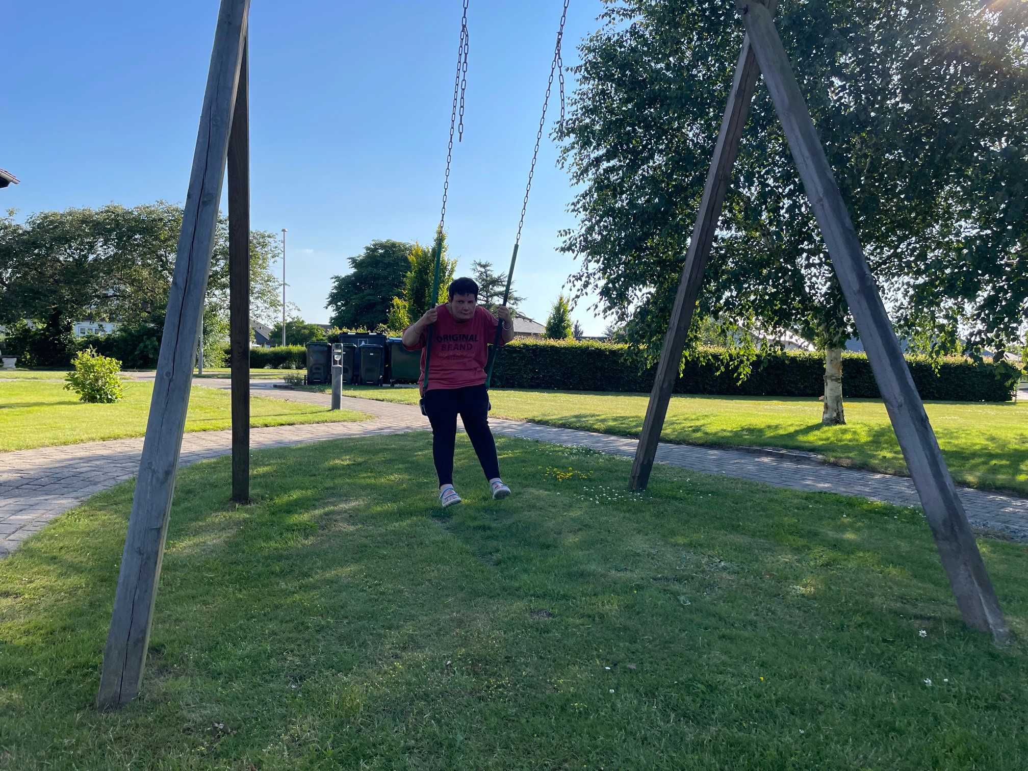 På den store græsplæne med flisegange gynger en borger på gyngestativet af træ