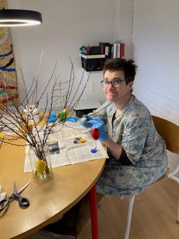 Borger sidder og maler påskeæg i forskellige farver, der står foran borgeren en vase med grene i. På disse grene skal de dekorede æg hænge på bagefter.