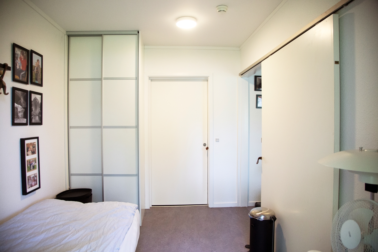 Soveværelse hvide vægge en seng med hvidt sengetøj på væggen er der billeder af mennesker