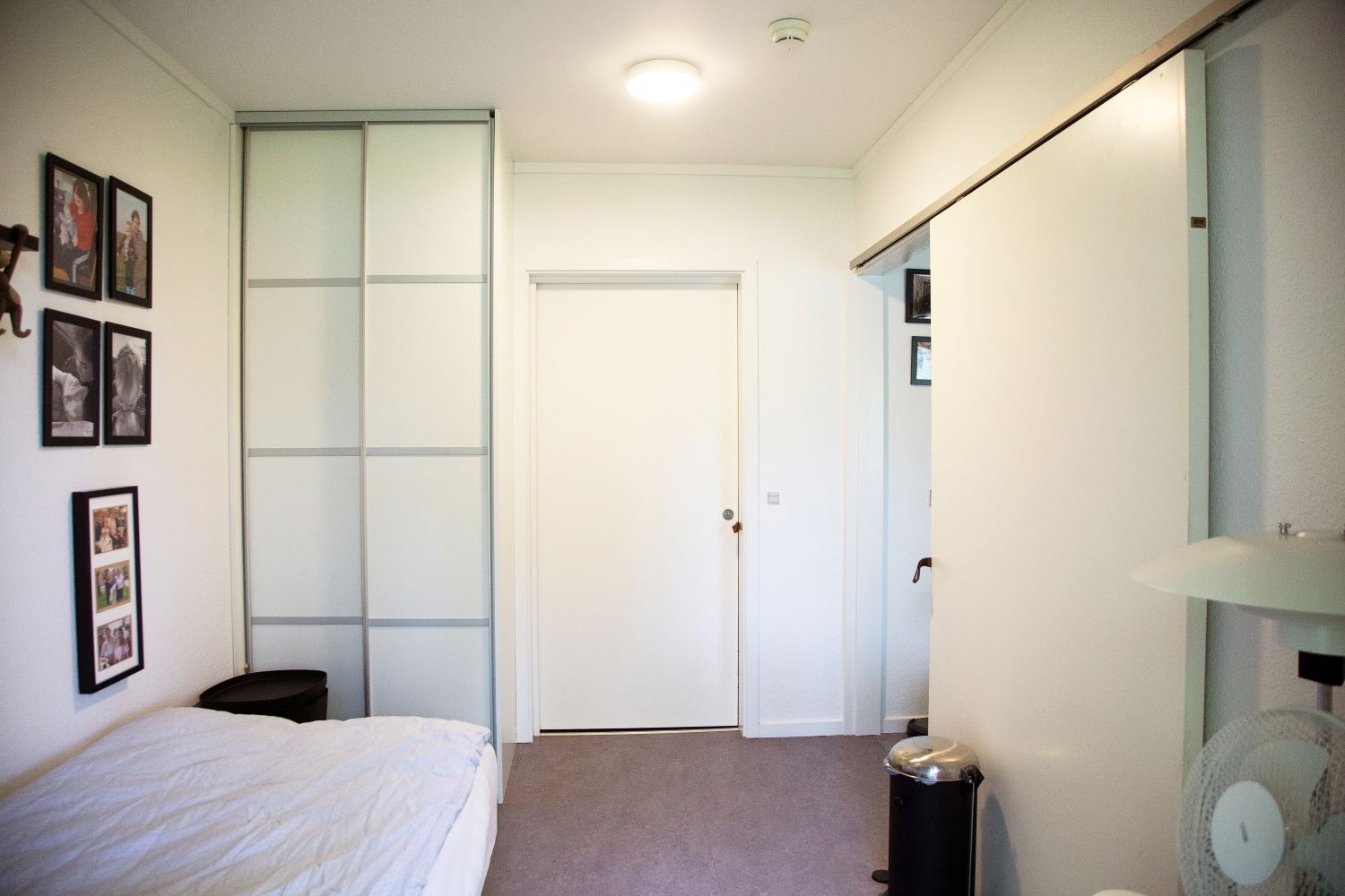 Soveværelse hvide vægge en seng med hvidt sengetøj på væggen er der billeder af mennesker