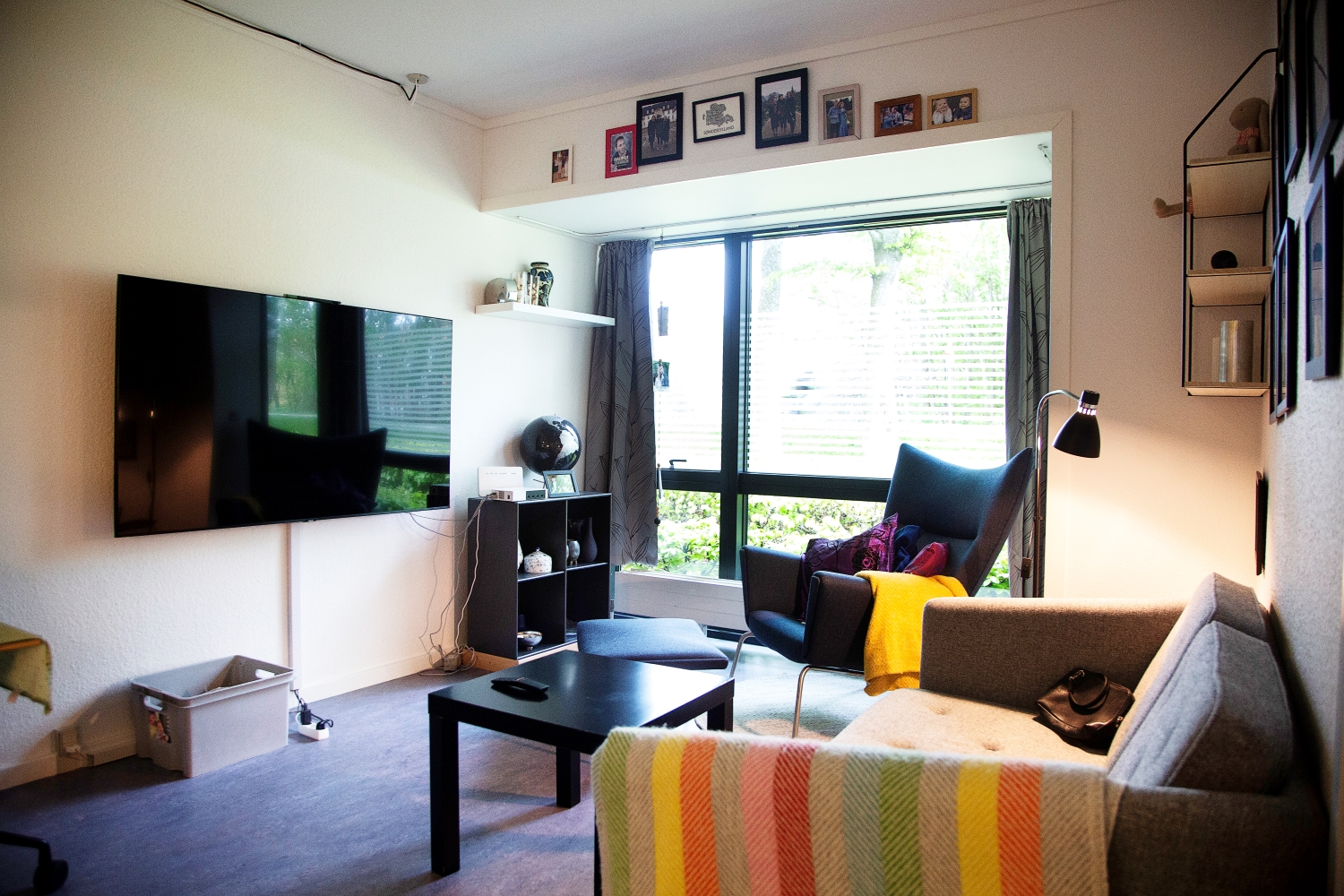 Dagligstue i en lejlighed blåt linoliumsgulv grå sofa i uld med forskelligfarvet tæppe sort lænestol med skammel 