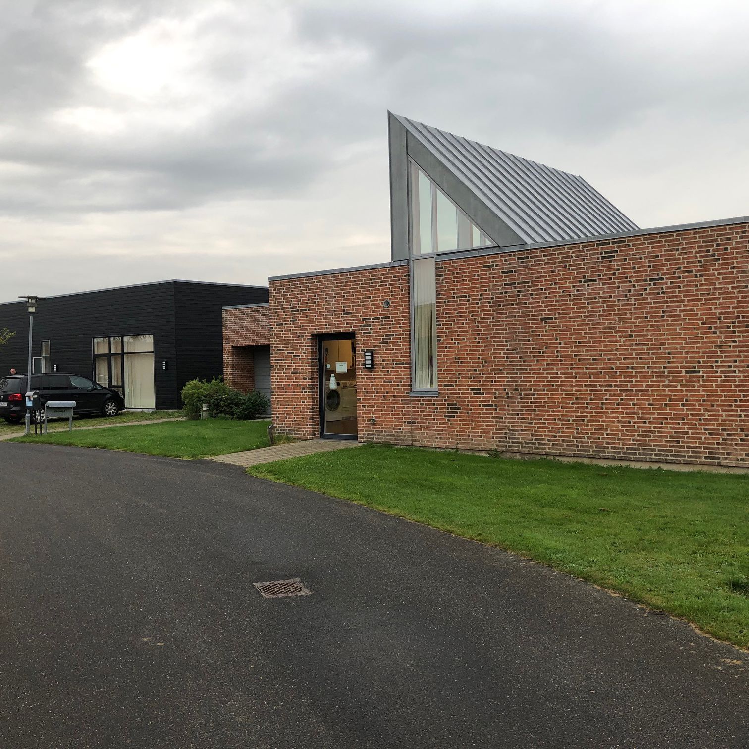 Æblevej 2 udefra. Bygninger er af røde mursten, og træ der er malet sort. Foran bygningerne er der en sti der fører ind til indgangen til Æblevej . Til højre i billedet står der en grå lygtepæl.